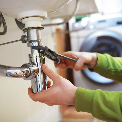 Hands adjust a chrome sink drainpipe with pliers beneath a bathroom basin, suggesting a focused, practical plumbing repair.