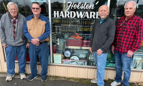 Four older men stand outside Holston Hardware, posing in front of the shop window; their relaxed expressions and workwear convey small-town camaraderie.